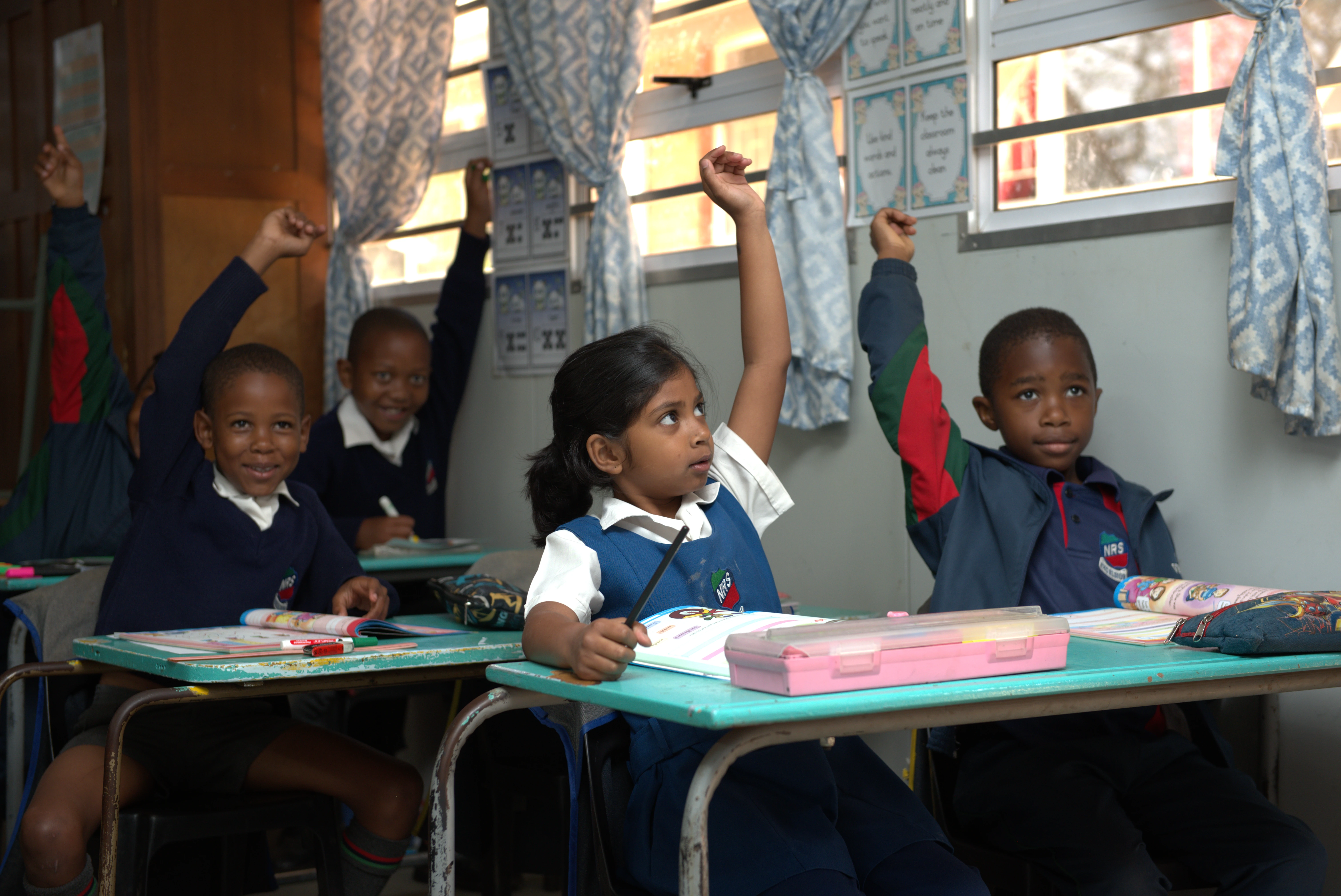 Foundation Phase learners participating with hands raised in class